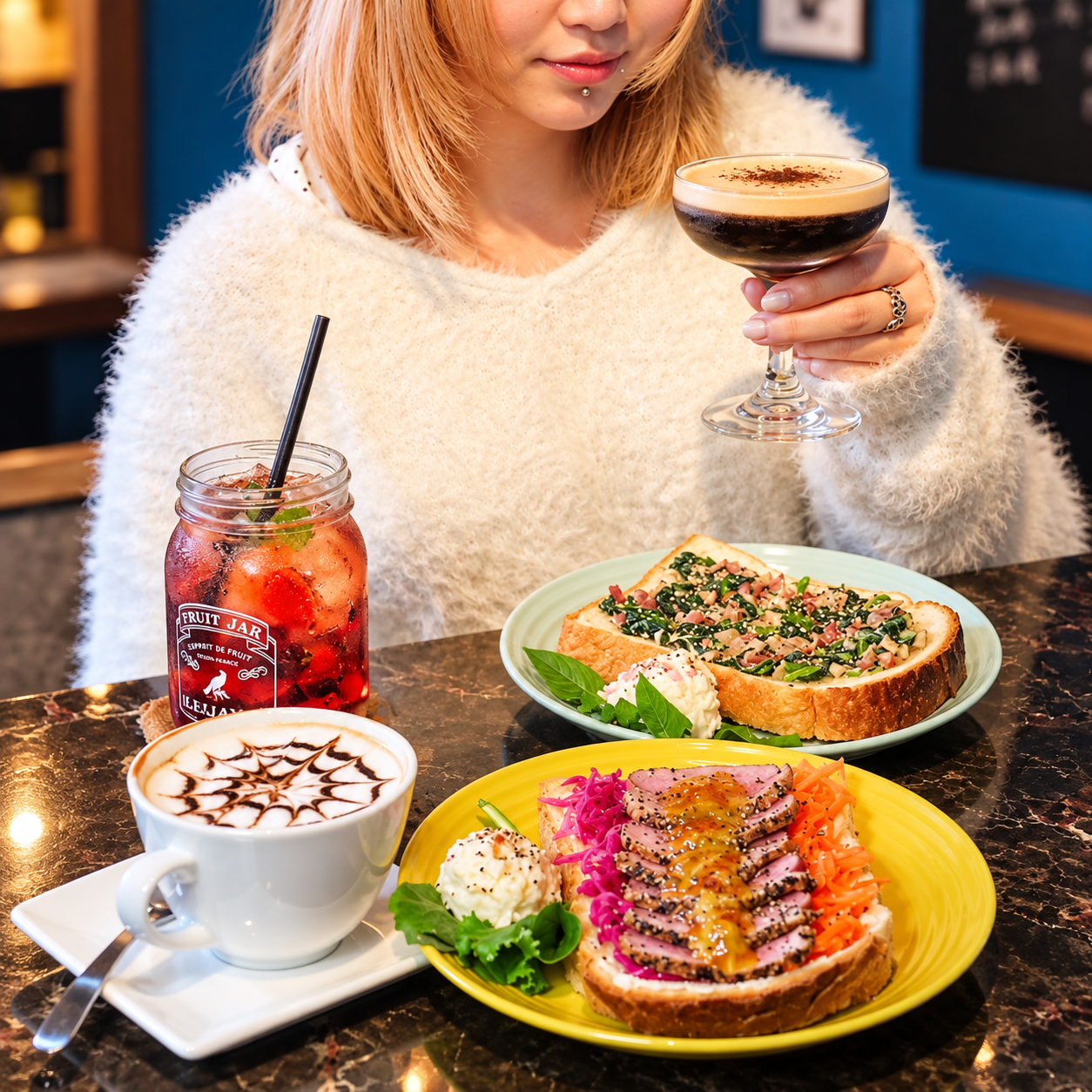エスプレッソマティーニを手にした女性と、フルーツジャーのドリンク、カプチーノ、鴨肉とほうれん草のトーストが大理石のテーブルに並ぶ様子